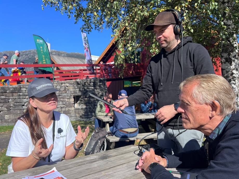 Programleder Rasmus og gjest Jannicke sitter ved et bord ute på Dyrsku'n. Tekniker Lars står med mikrofonen.