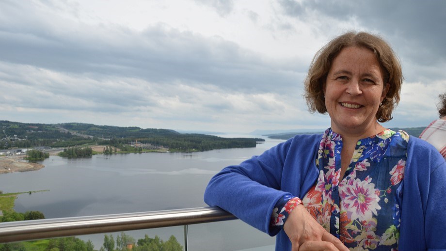 Elisabeth Gjems står vendt mot kamera og smiler. Bakgrunnen viser utsikt mot Mjøsa.