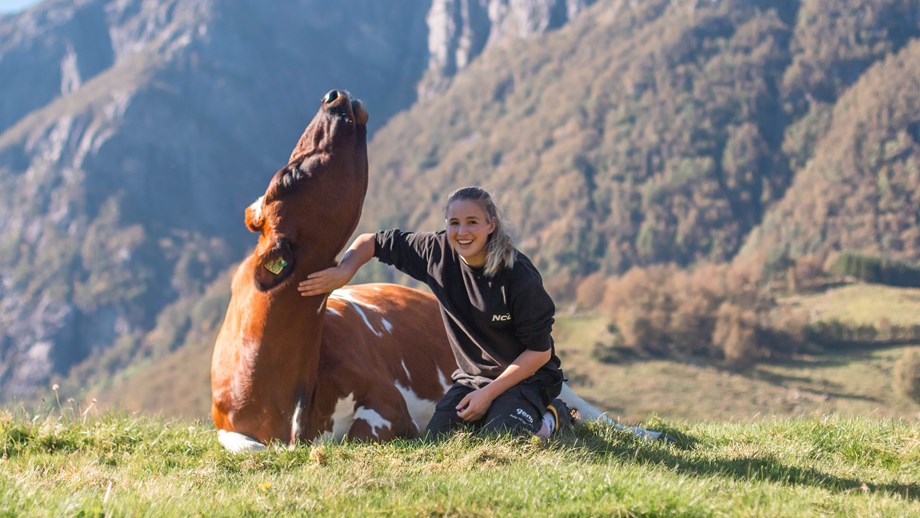 Nora Sandberg sitter på huk i snøen sammen med en kalv. Snødekket jorde og blå himmel i bakgrunnen